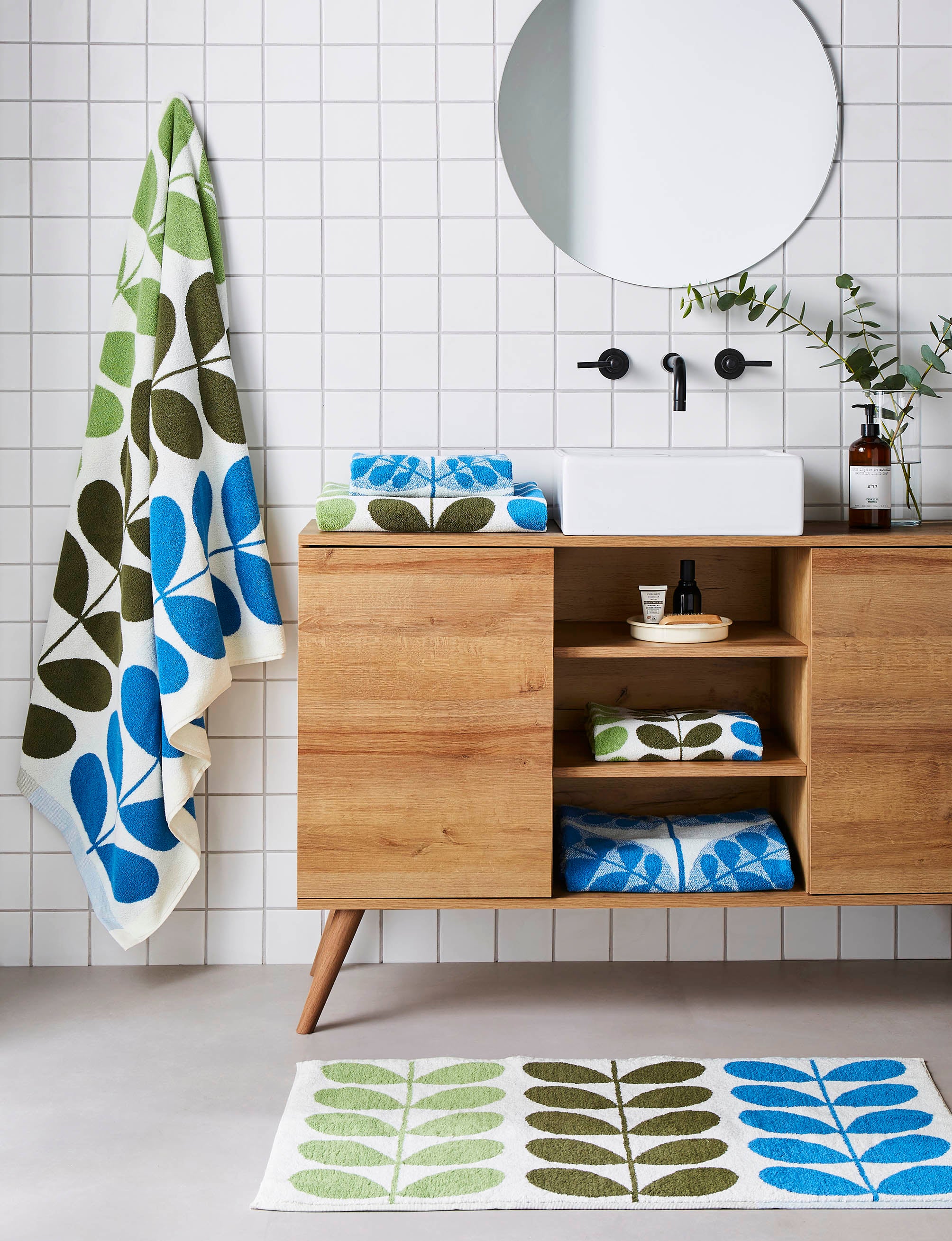 Colourful towels and bathmat in blues and greens in a neutral bathroom setting