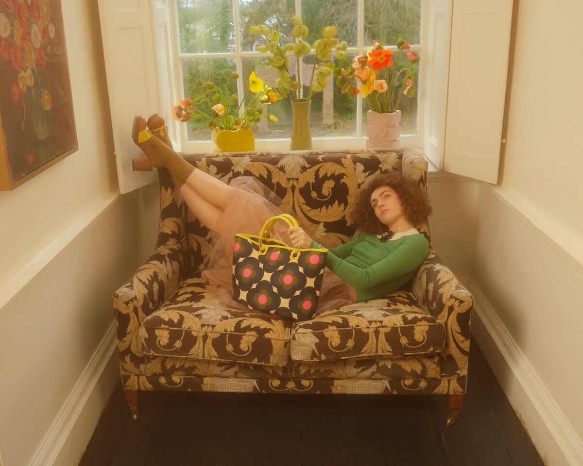 Model reclining on chair with Orla Kiely smile tote bag 