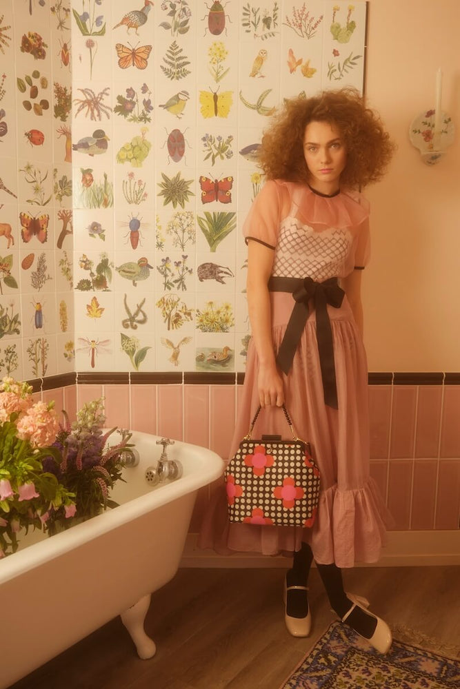 Model holding an Orla Kiely Jenny D bag next to a bath full of flowers