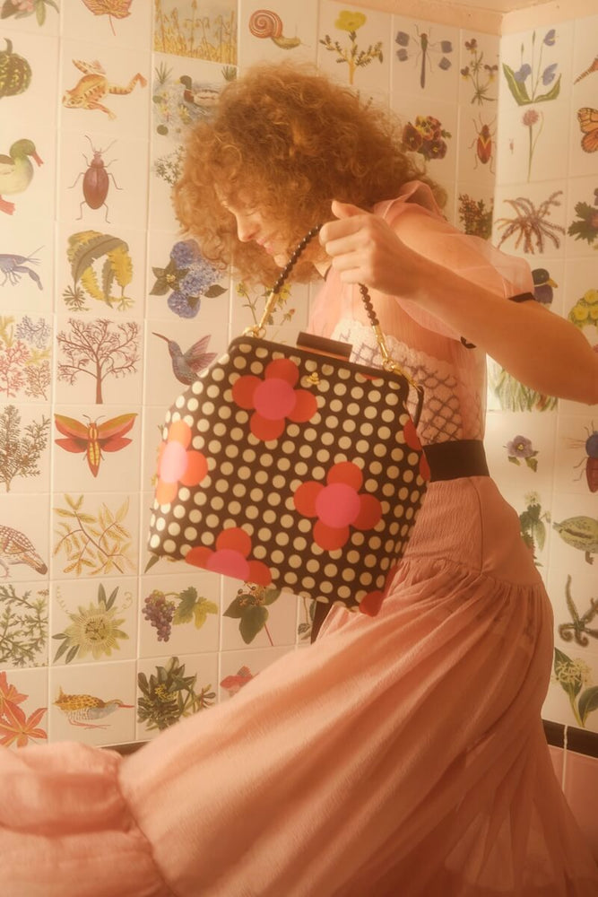 Model holding a Satin Orla Kiely bag in front of tiles depicting nature