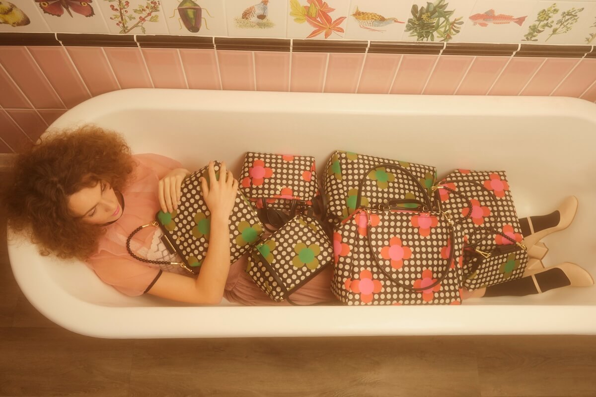 Model in bath tub filled with satin Orla Kiely bags