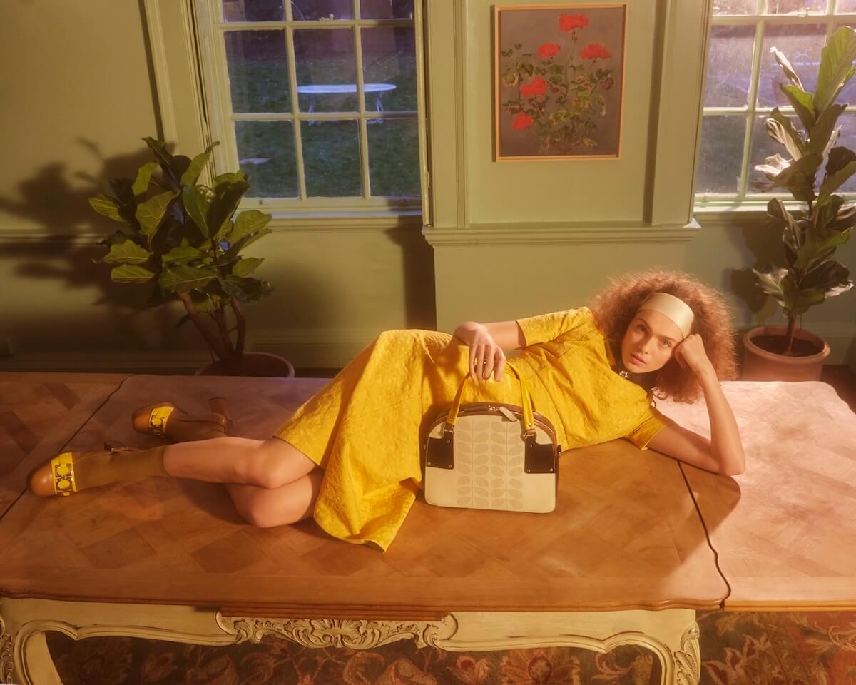 Model posing on a table with a leather Orla Kiely bag 