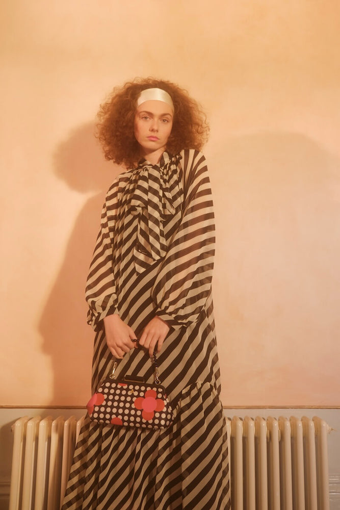 Model with curly hair holding a satin Orla Kiely handbag