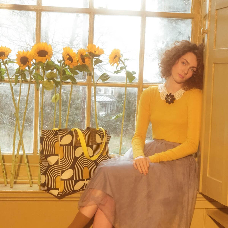 Model in window with flowers and Orla Kiely tote bag 