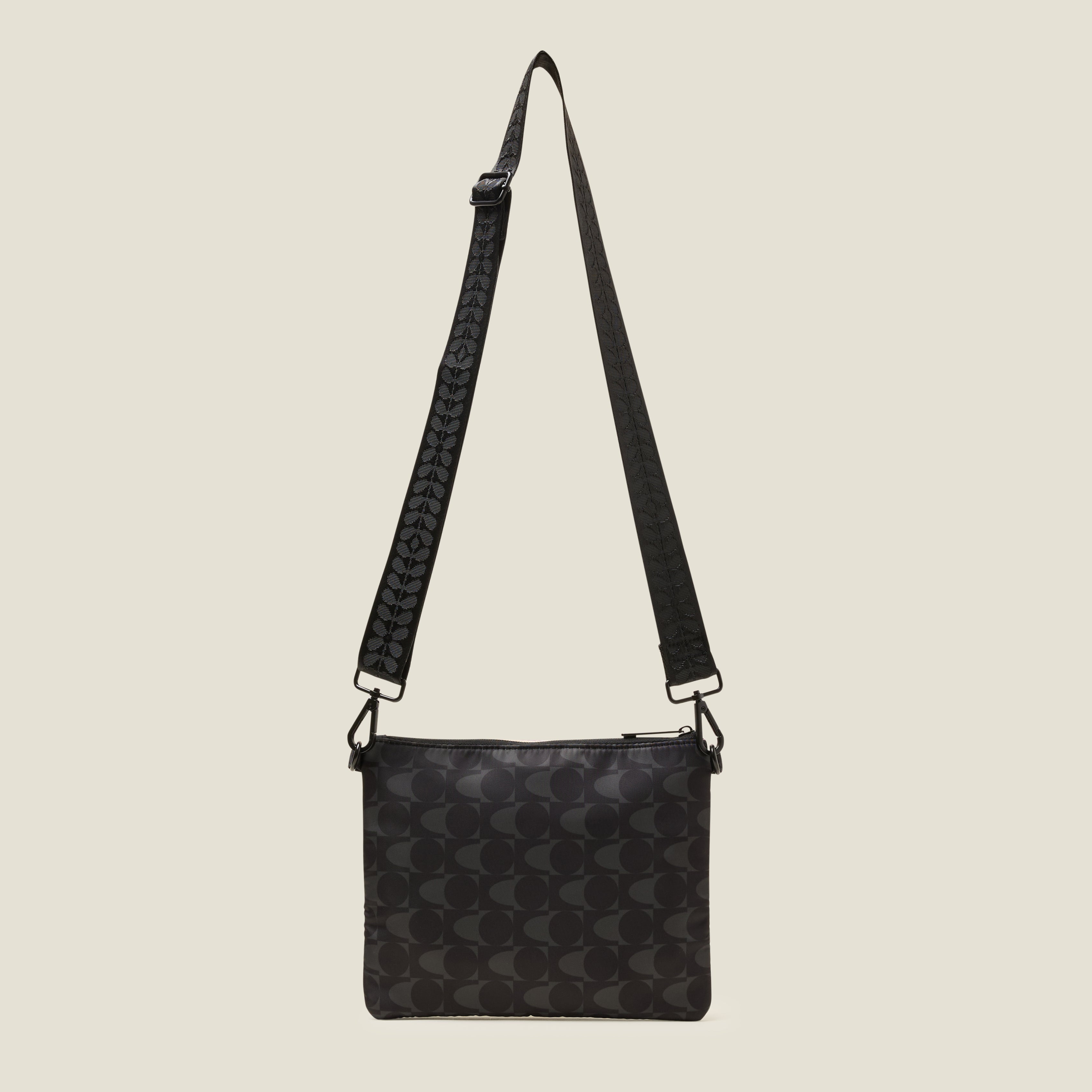 Flat lay of a Black and grey patterned crossbody bag with the webbing strap at full length on a beige background