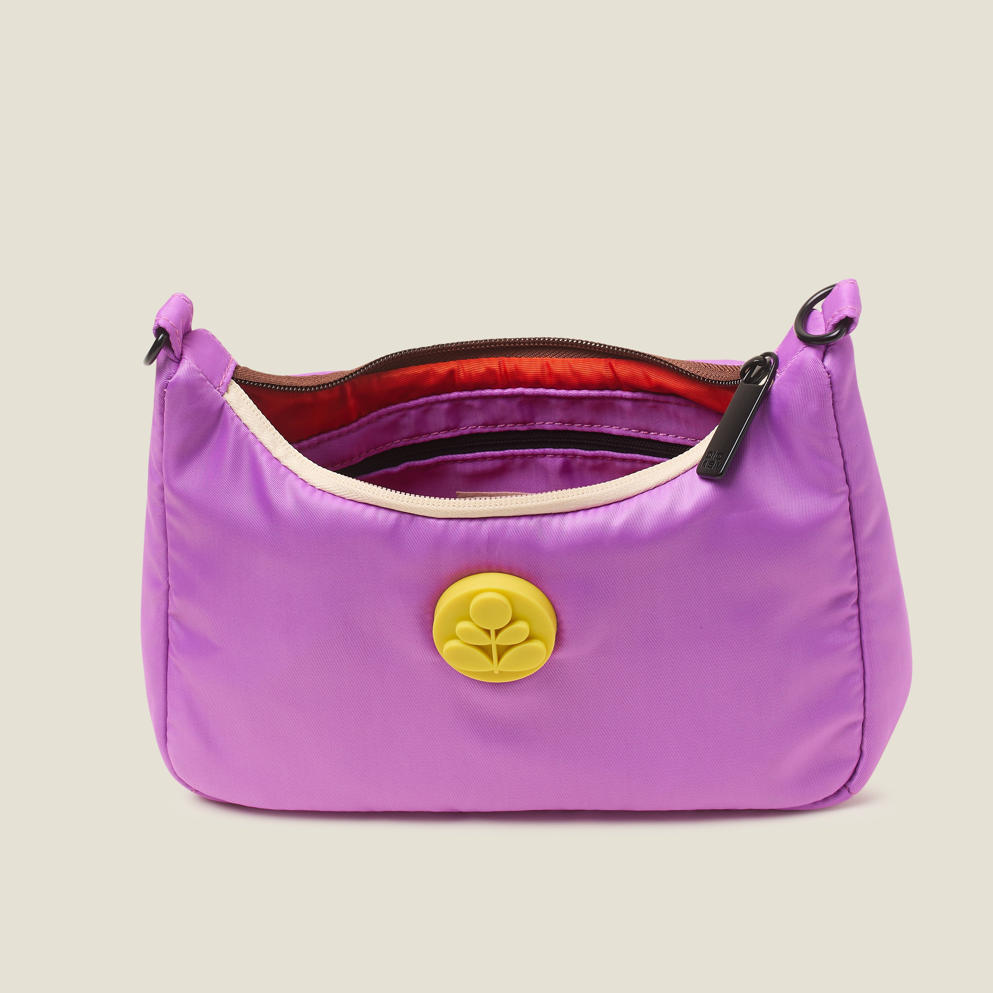 A close up view of a handbag in lilac purple, featuring a yellow rubber Orla Kiely stem logo with brown carry handles on a beige background