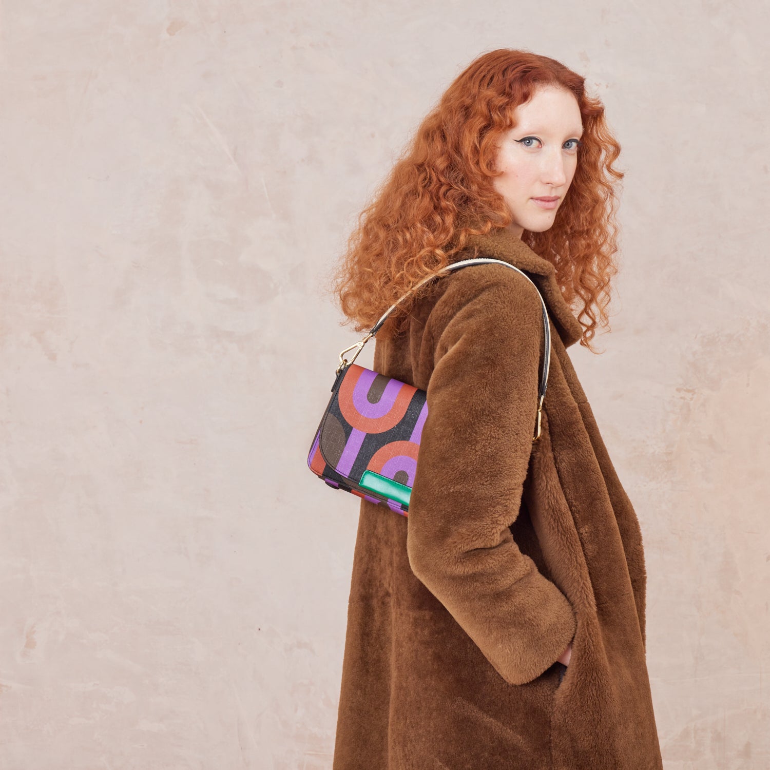 Woman in a brown coat wears a colourful retro print handbag over her shoulder.