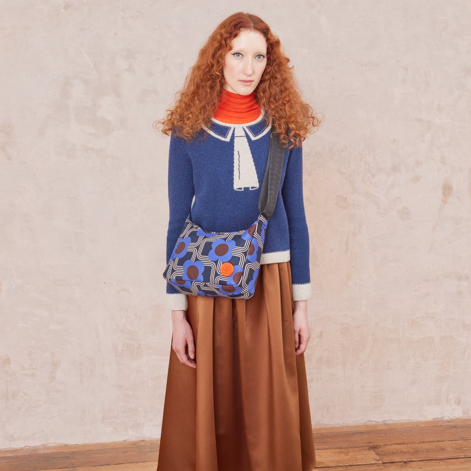 A woman wears the small crossbody hobo bag, in our colbalt blue pattern with orange stem logo branding.