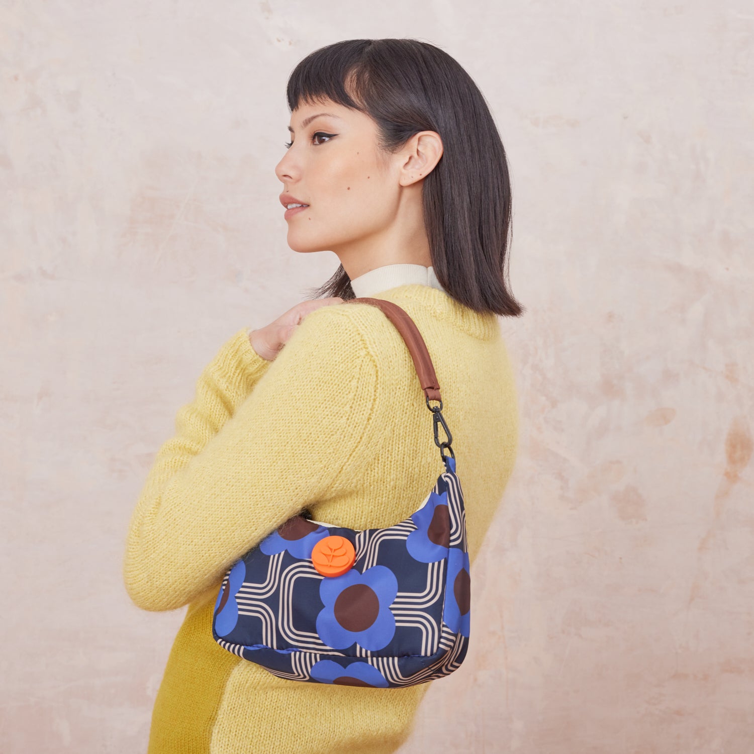 Woman wearing a yellow sweater with the Venn handbag using the detachable over the shoulder strap, the bag is in a blue floral-pattern.