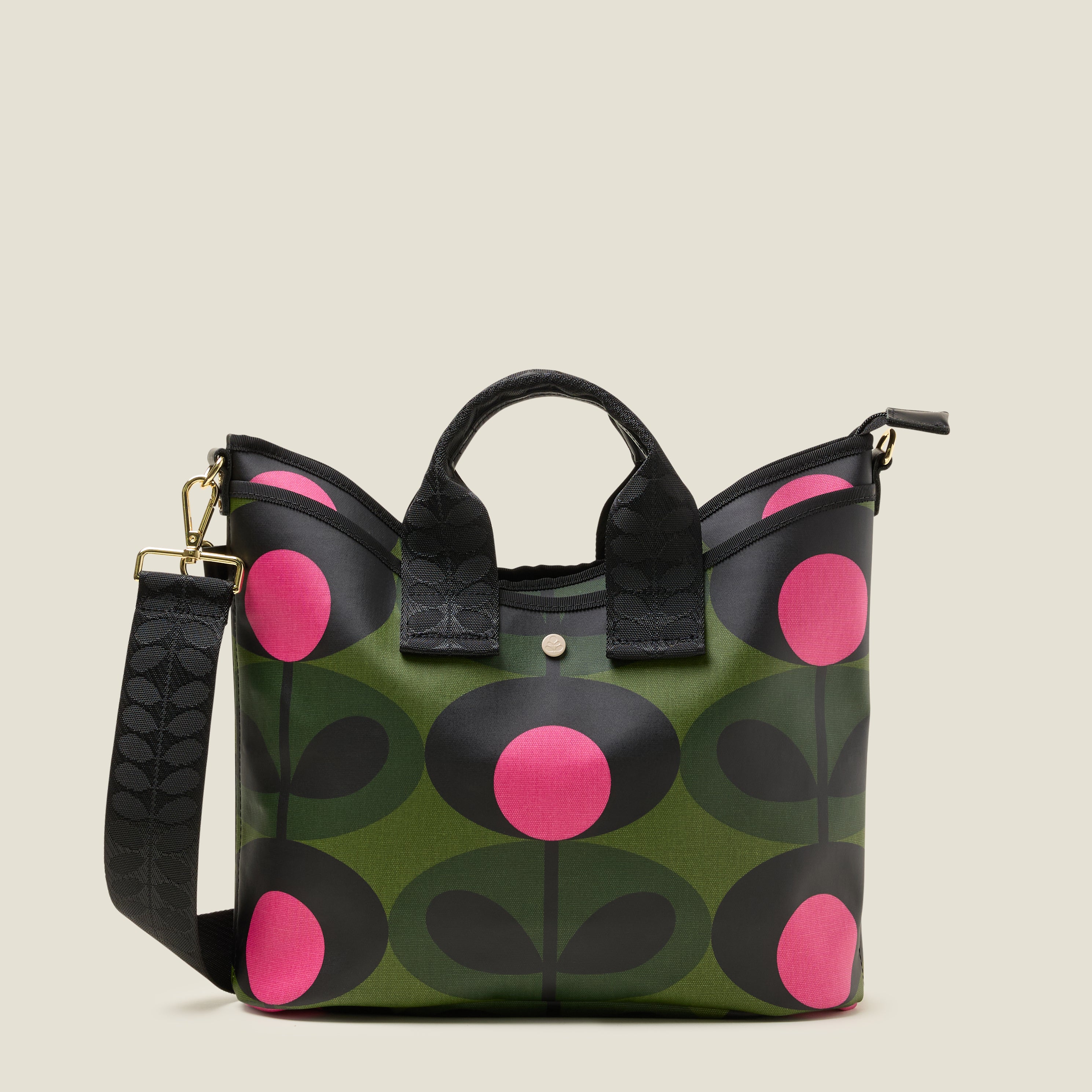 Crossbody bag in forest green print with pink dots, featuring a front slip pocket and branded grab handles and strap.