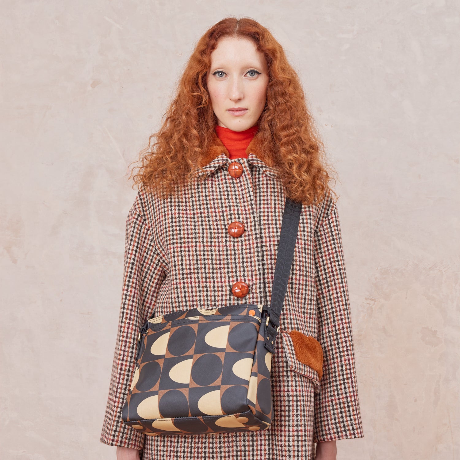 Woman wearing a plaid coat with the Fielder crossbody bag in a brown and cream pattern.