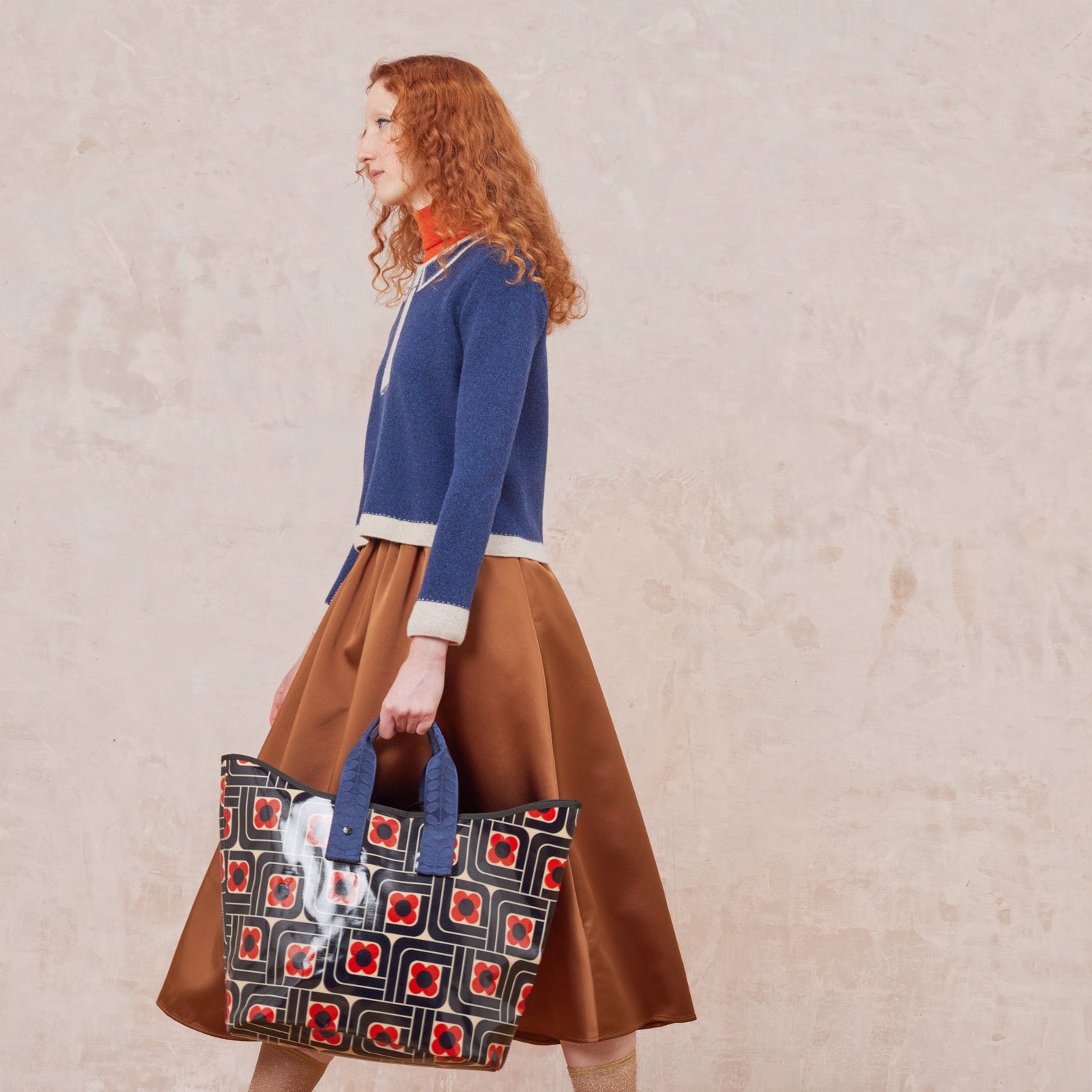 Woman holding a large patterned tote bag in navy, red and cream in a floral woodblock print.