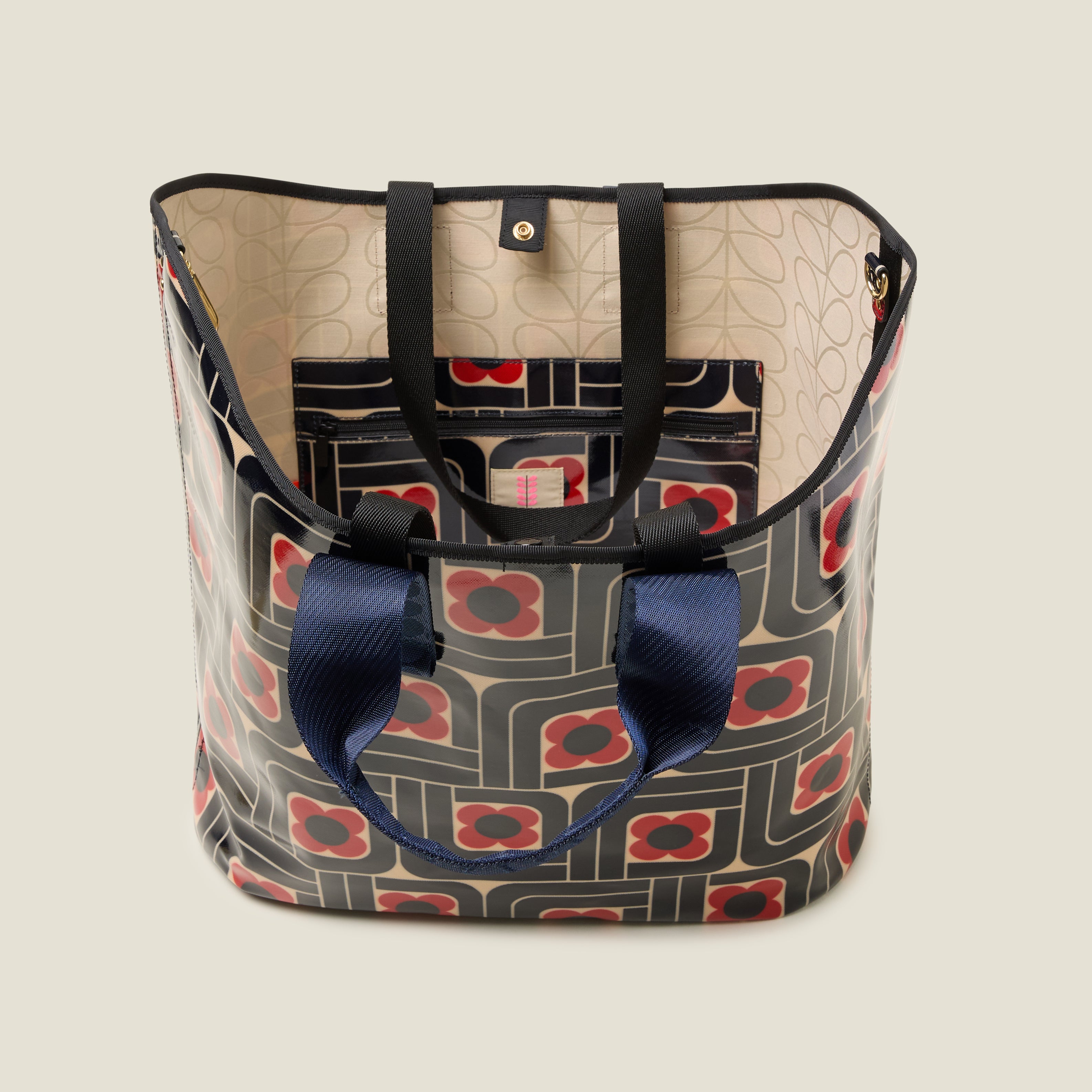 Top view of large patterned tote bag with red, navy and cream woodblock design, with navy grab handles. Inside features a zip pocket and snapper fastening.
