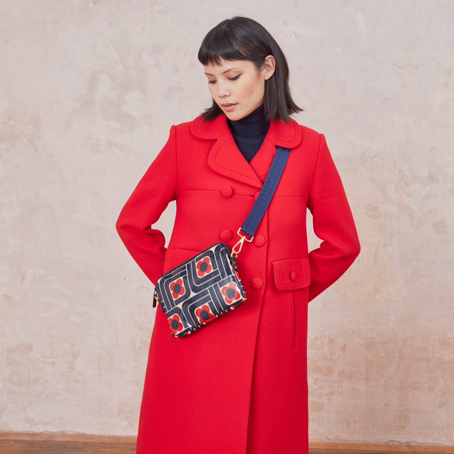 Woman in a red coat wearing the slim crossbody patterned handbag in navy, red and cream.