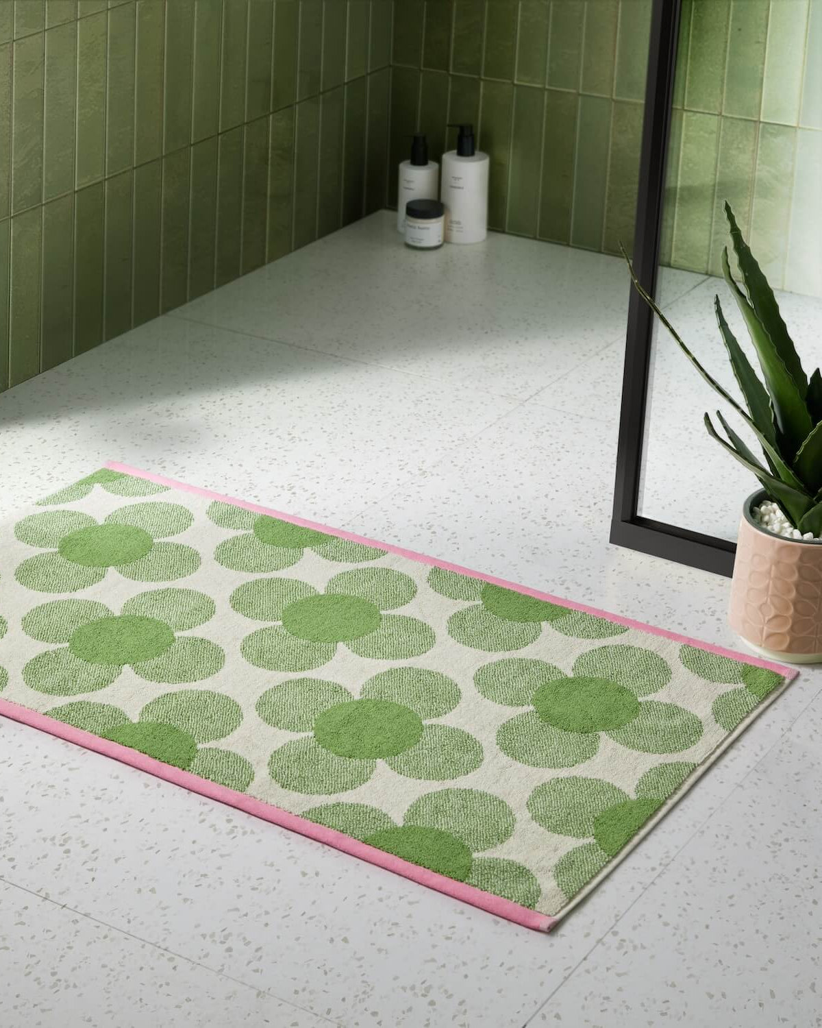 Lifestyle shot of the retro flower clover green Orla Kiely bathmat next to a shower