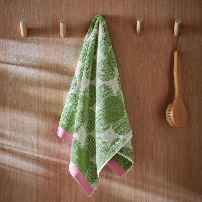 Lifestyle shot of retro flower green Orla Kiely towel hanging from hook