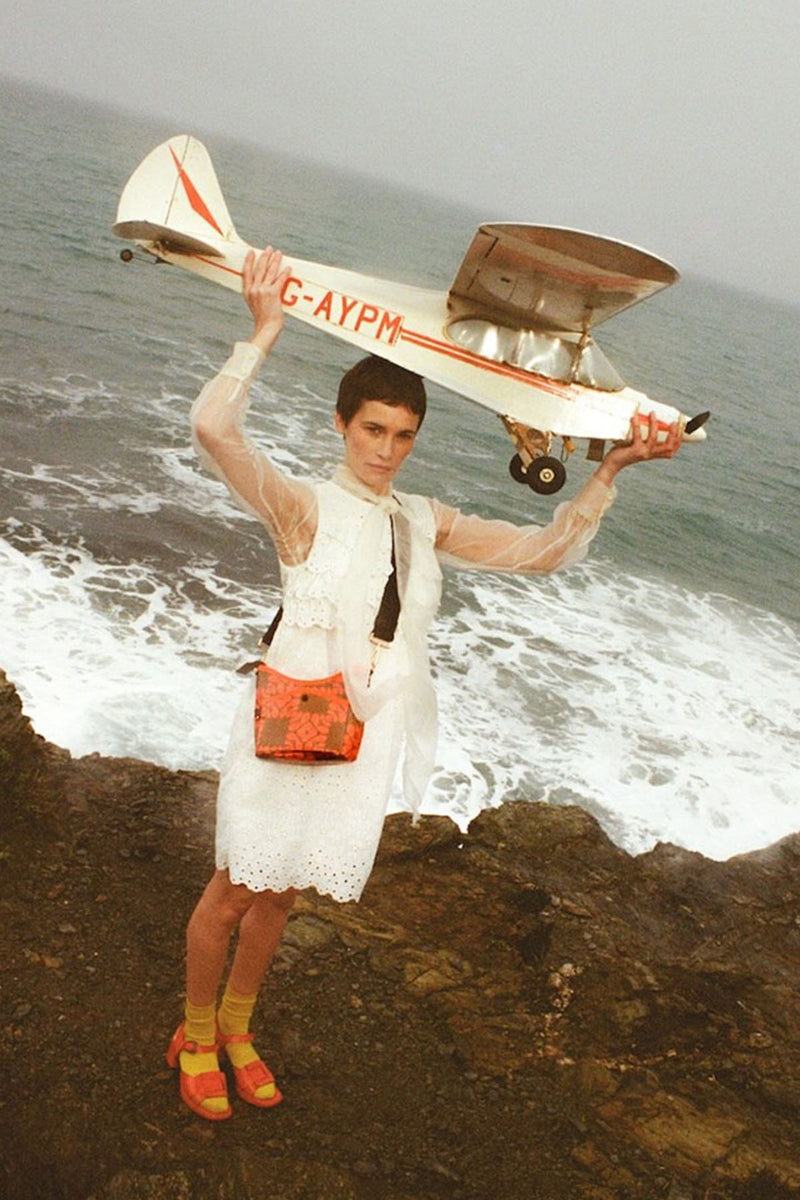 Model with Orla Kiely crossbody bag holding a plane on the beach 