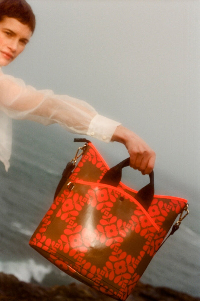 Model holding a glossy Orla Kiely bag by the ocean