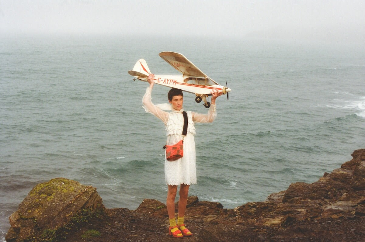 Model with Orla Kiely crossbody bag holding a plane on the beach 