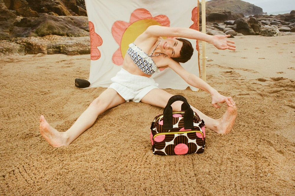 Model stretching on beach with Orla Kiely handbag 