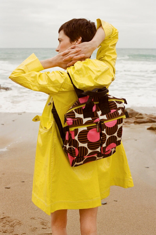 Model in yellow coat with Orla Kiely backpack with pink striped flowers