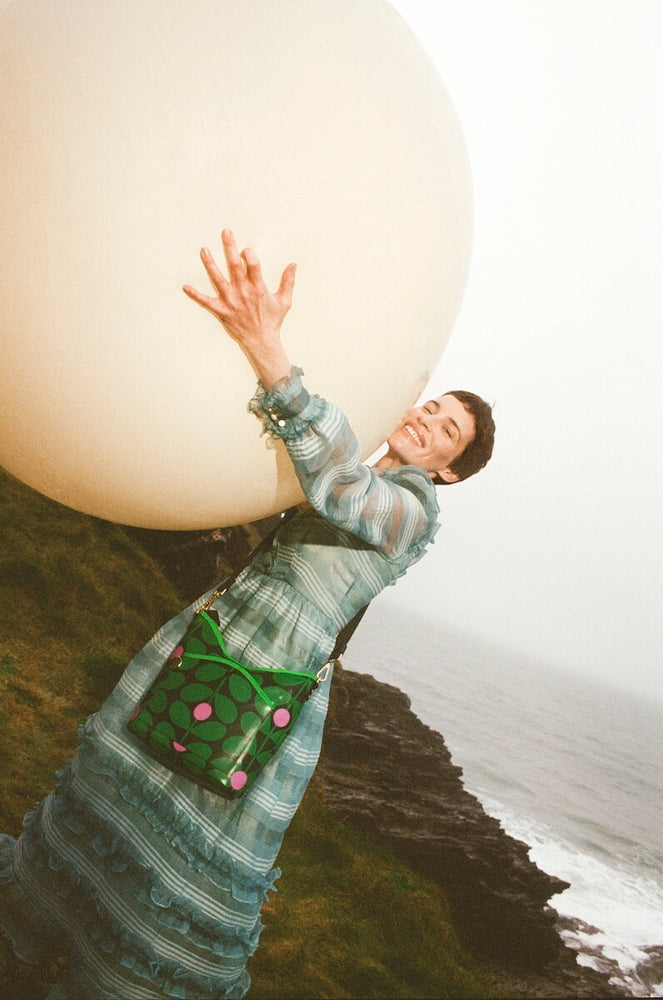 Model hugging a giant ball whilst wearing a crossbody Orla Kiely bag 