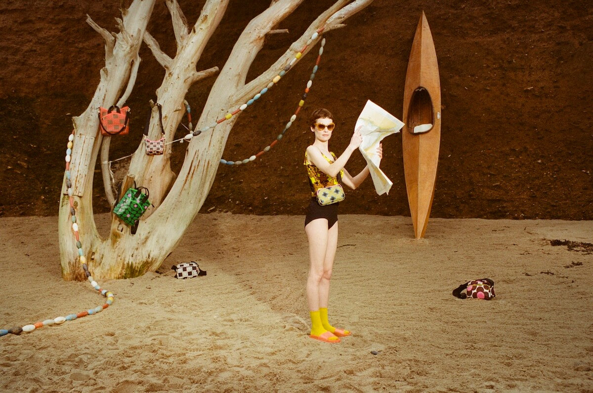 Model on the beach with a canoe and Orla Kiely bags