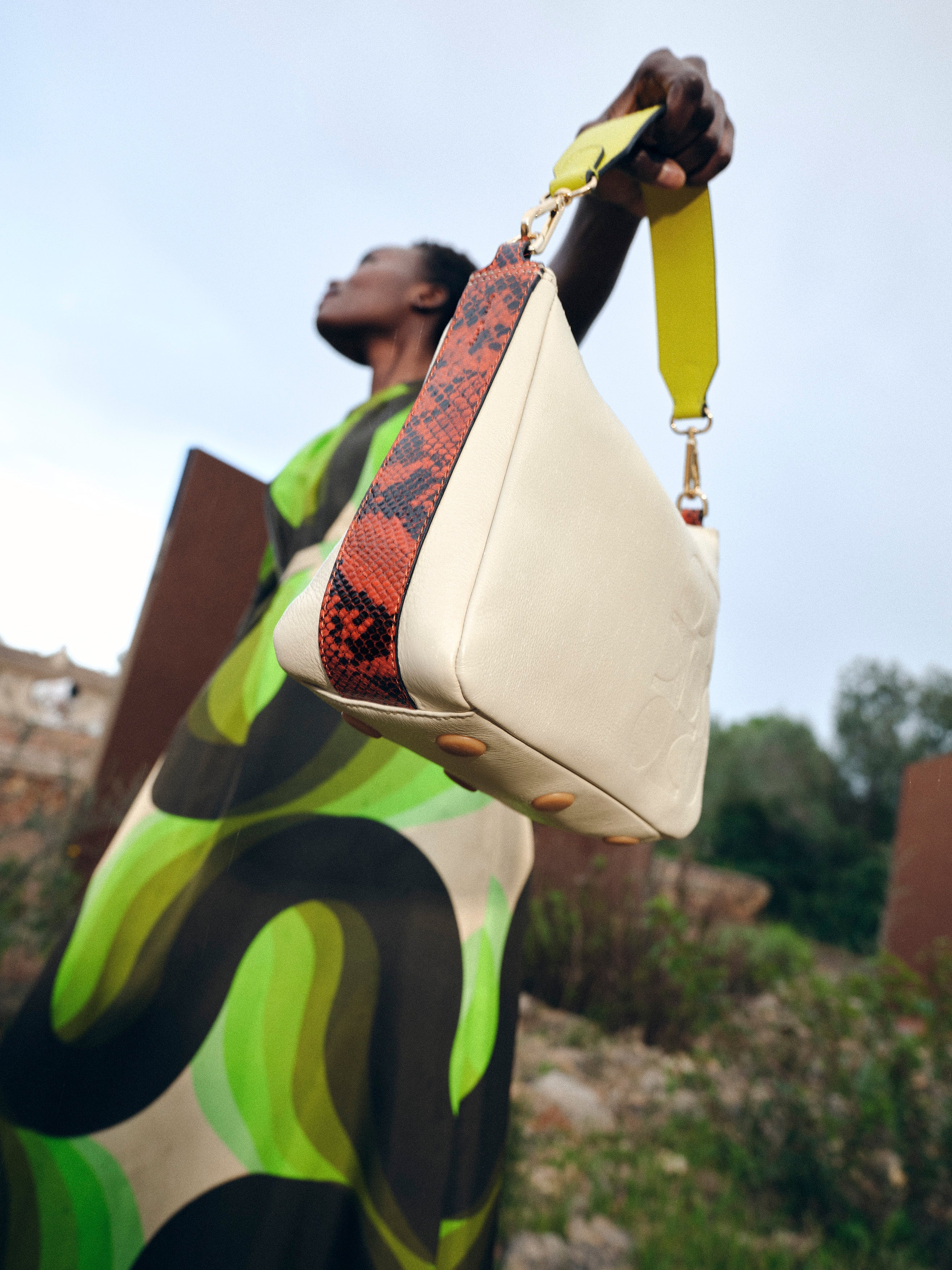 A women in a yellow dress sits on a chair holding a leather handbag by Orla Kiely 