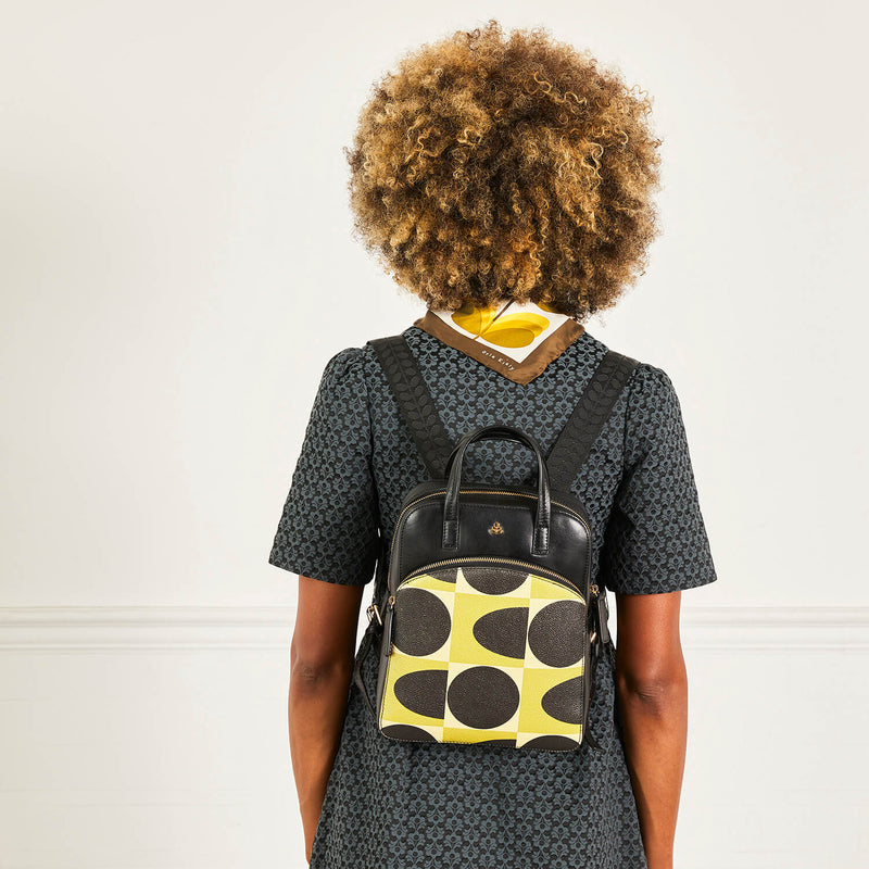 Model wearing an Orla Kiely Emilia Leather Backpack in Chestnut Spot Square