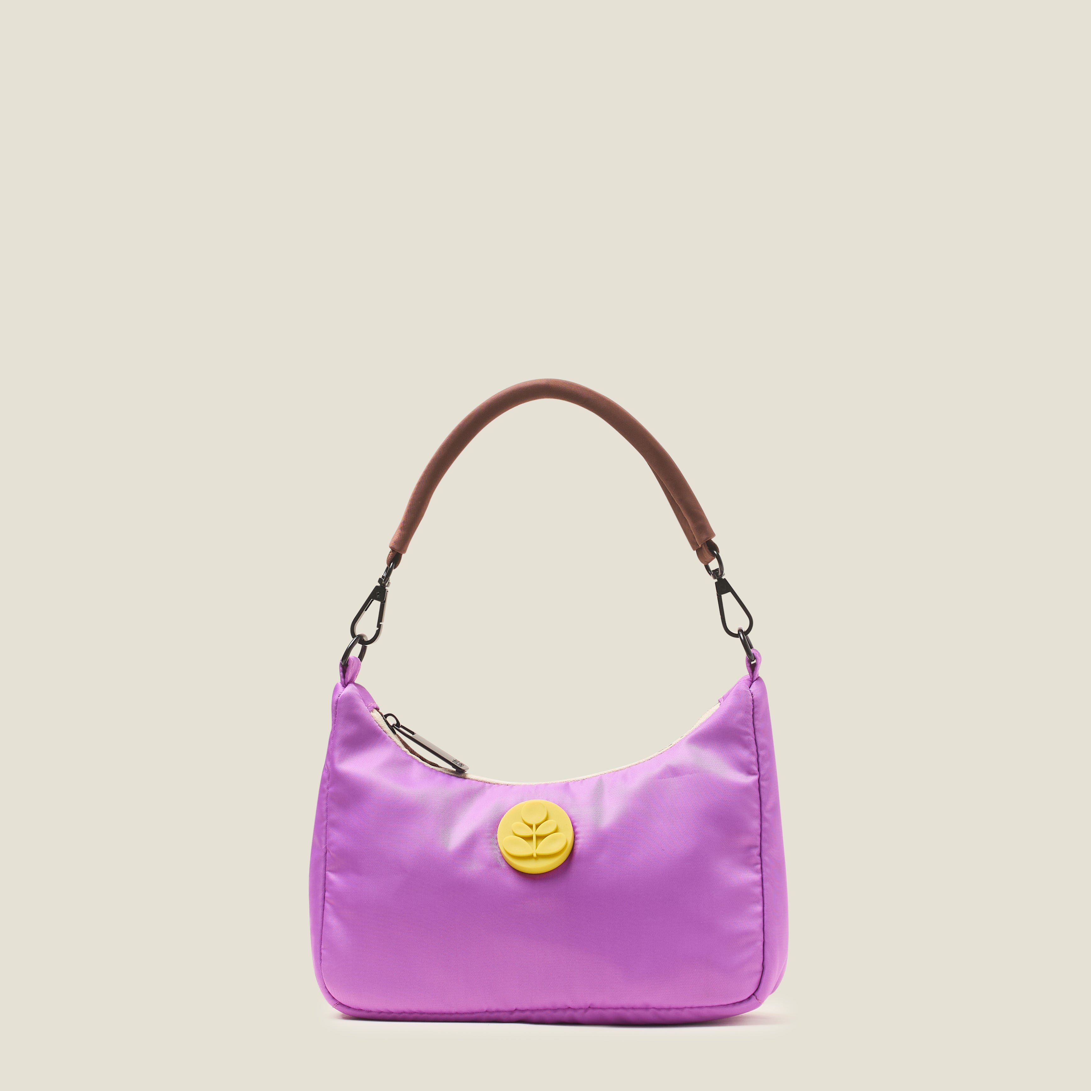 Front view of an over the shoulder handbag in lilac purple, featuring a yellow rubber Orla Kiely stem logo with brown carry handles on a beige background
