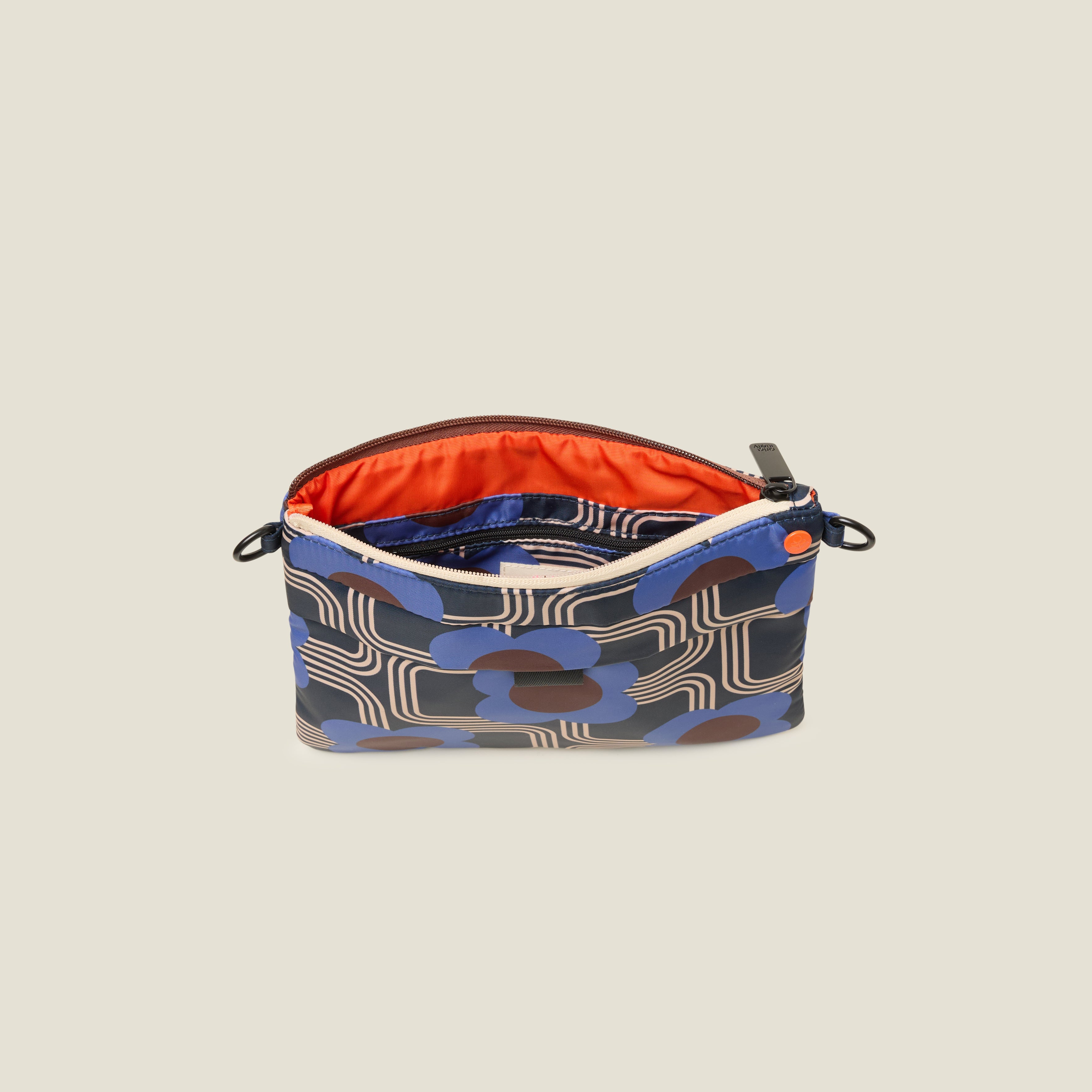 The crossbody strap is removed to create a clutch style bag that features a navy blue, cobalt blue and cream geometric pattern is open to reveal the orange lining.