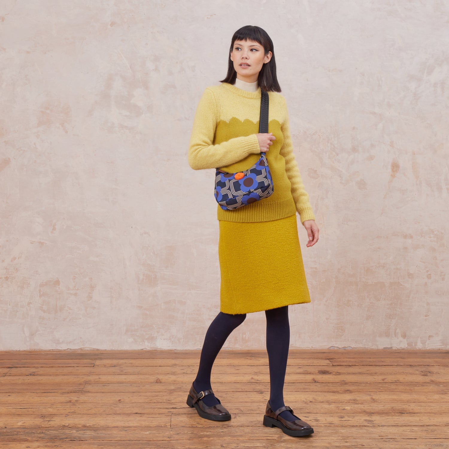 Woman wearing a yellow sweater with the Venn handbag using the detachable and adjustable crossbody strap, the bag is in a blue floral-pattern.
