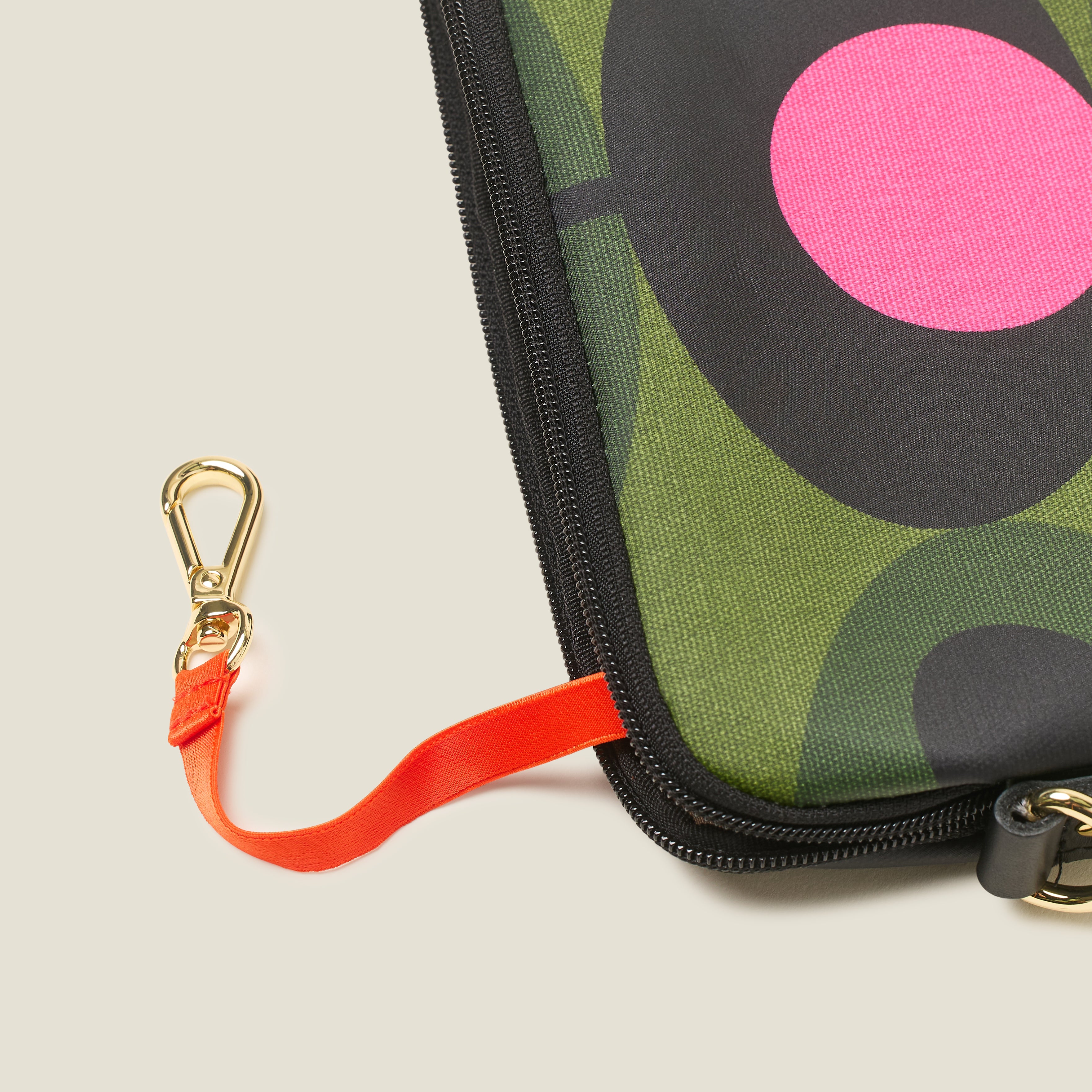 Detail of green patterned slim crossbody bag with a pink flower, zip closure and key chain.