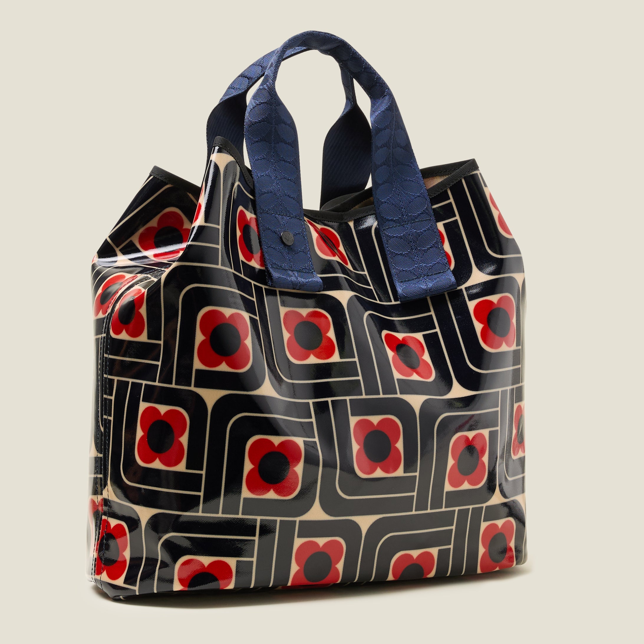 Side view of large patterned tote bag with red, navy and cream woodblock design, with navy grab handles, and top corners folded in for more security.