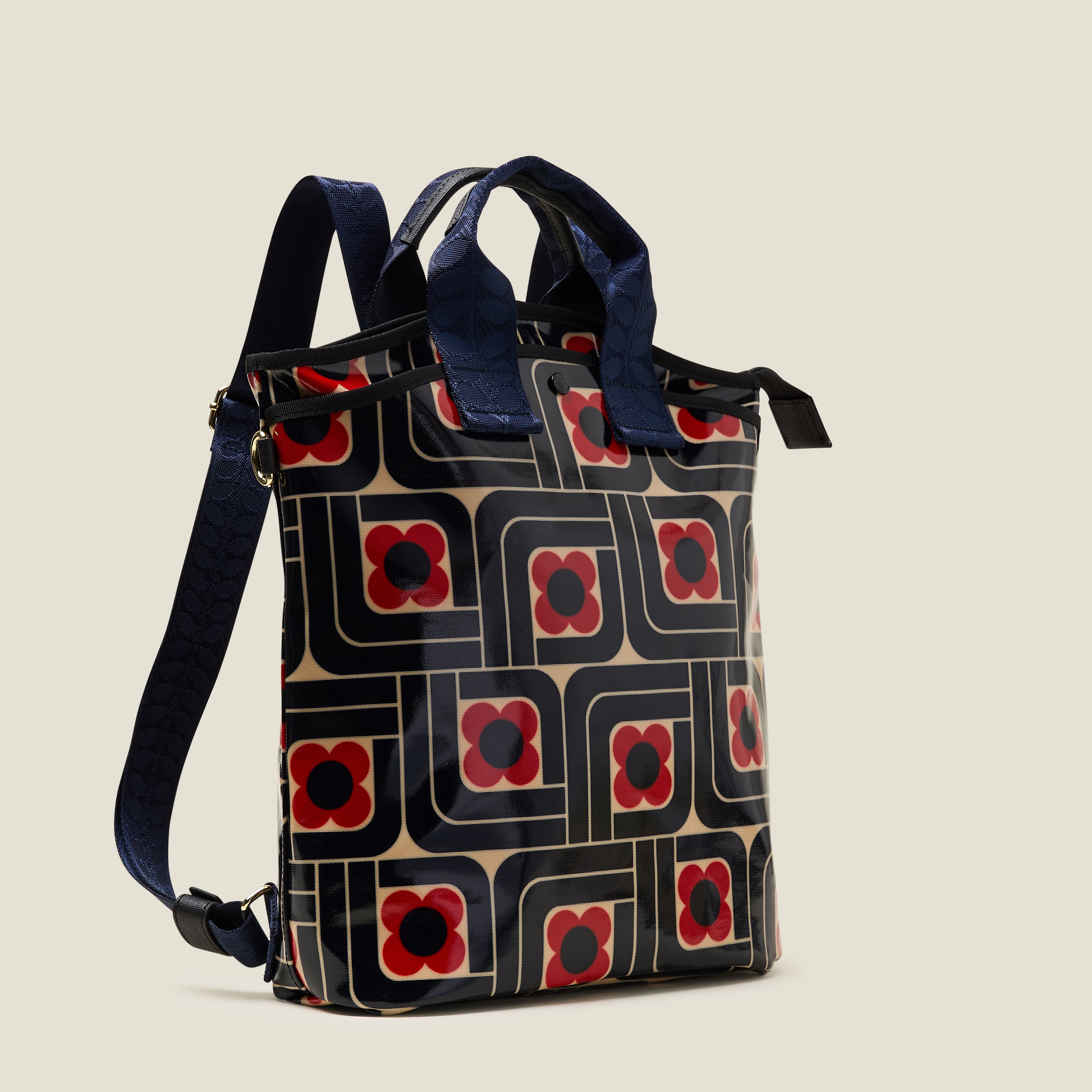 Side view of a women's backpack in a navy blue and red geometric floral pattern, with webbing grab handles and straps on a beige background.