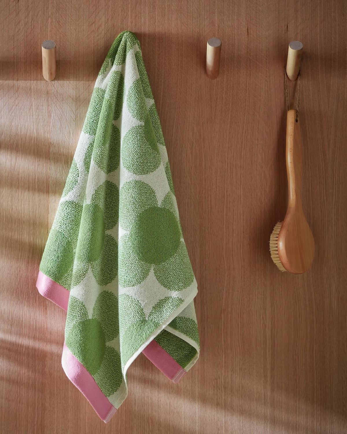 Lifestyle shot of retro flower green Orla Kiely towel hanging from hook