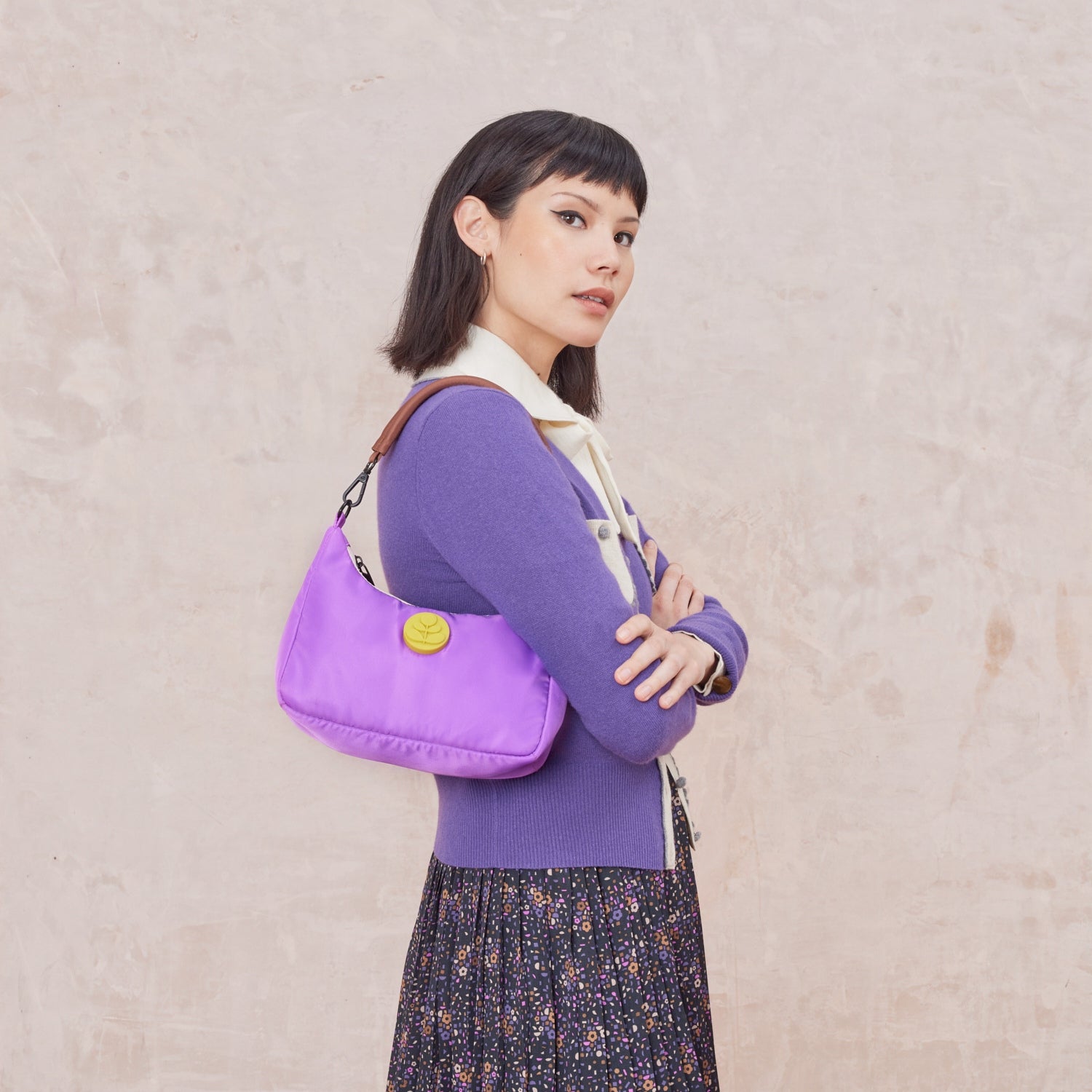 Over the shoulder lilac purple handbag, with yellow rubber Orla Kiely stem motif logo against a beige background