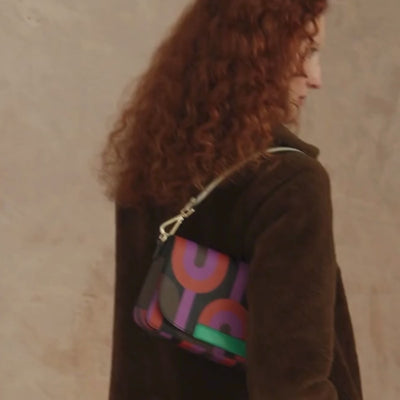Woman in a brown coat wears a colourful  retro print handbag over her shoulder during a pohotshoot.